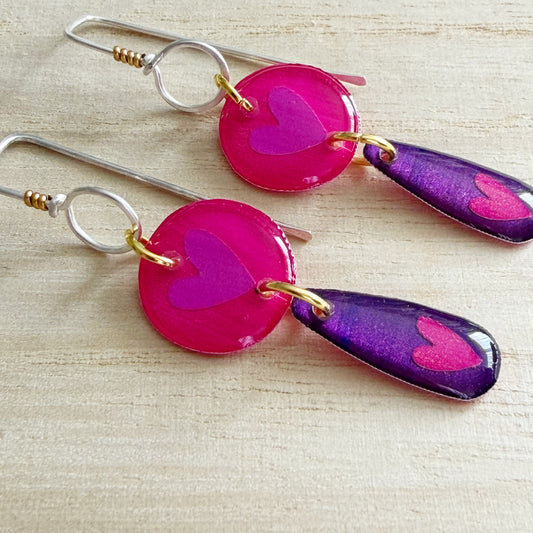 Pair of earrings with pink and purple heart-shaped drops on a wooden surface