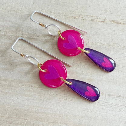 Pair of earrings with pink and purple heart-shaped drops on a wooden surface