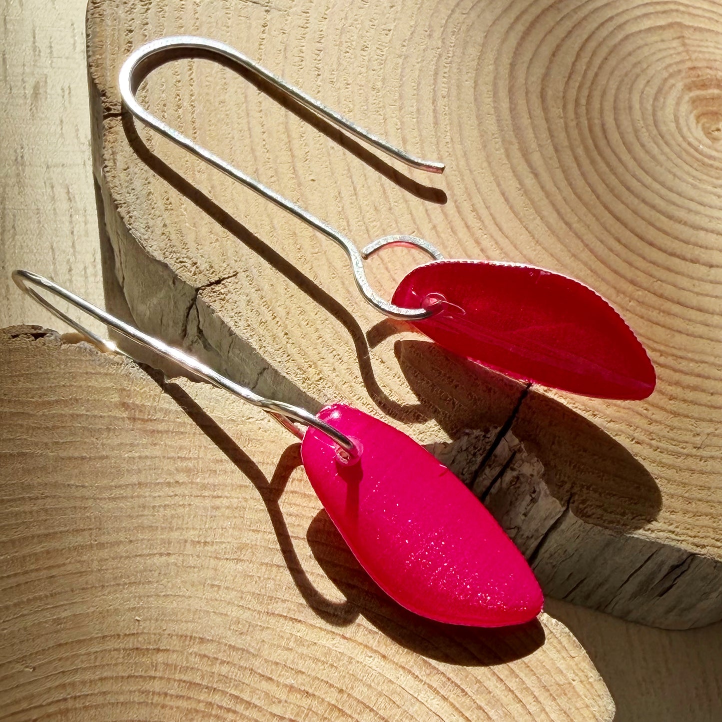 Pink coloured organic teardrop shaped drop earrings on wooden surface